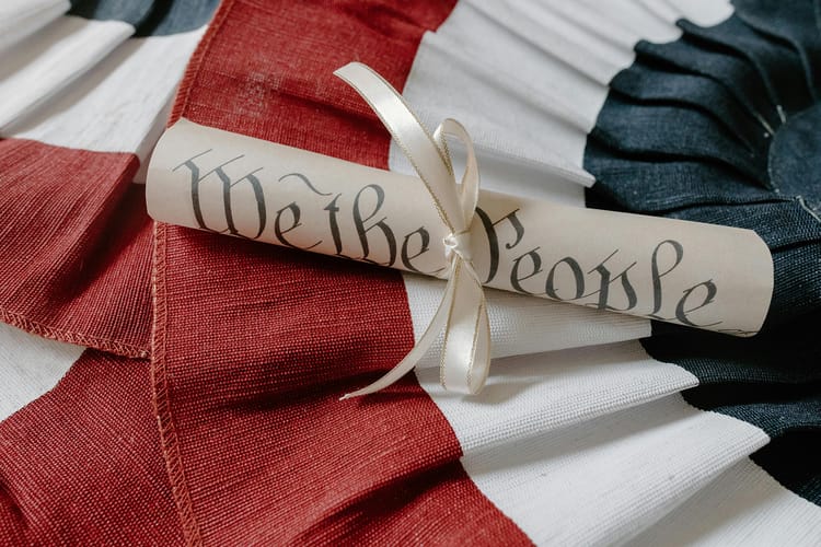 Paper titled We the People rolled up and tied with ribbon laying over red, white and blue cloth.
